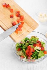 Female hands adding pieces of salmon into bowl with salad, close-up