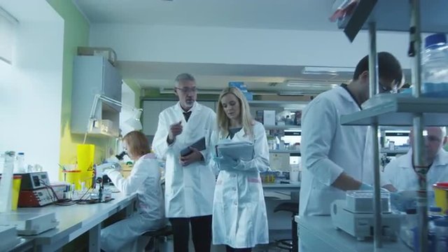Senior and female scientists with papers and tablet are walking and having a conversation in a laboratory.  Shot on RED Cinema Camera.