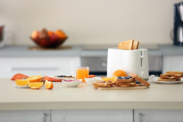 Toaster with dishes, sandwiches and oranges on a light kitchen table