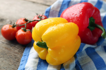 Pepper with tomatoes on striped cotton napkin against wooden background, close up