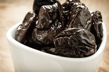 dried plums prunes in white bowl on wooden table