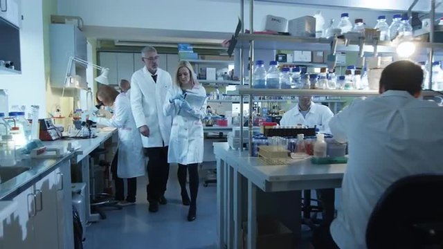 Senior and female scientists with papers are walking and having a conversation in a laboratory.  Shot on RED Cinema Camera.