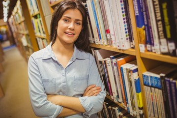 Smiling student standing next to bookshelves with arms crossed
