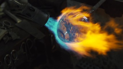 A glassmaker uses a blow torch to shape and form a glass object.