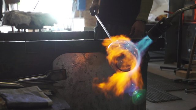 A glassmaker uses a blow torch to shape and form a glass object.