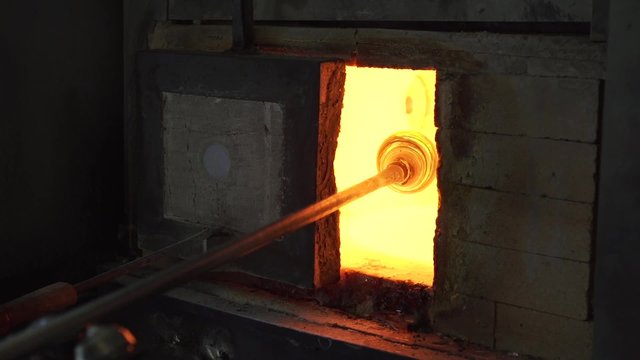 A glassmaker fires glass in a furnace.