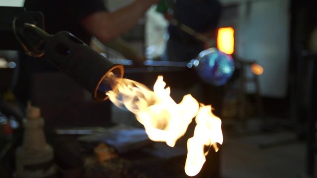A glassmaker uses a blow torch to shape and form a glass object.