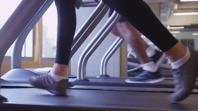 Close up of two people feet running on treadmill in gym low angle view