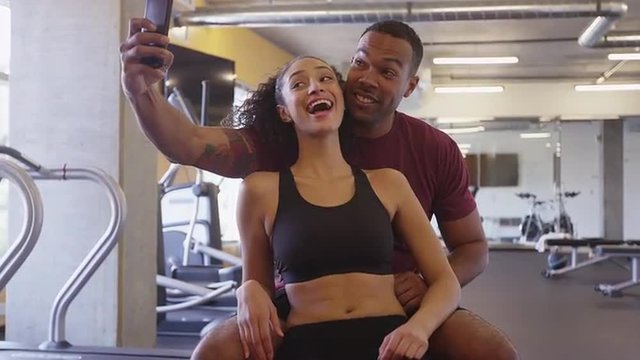 Cute Black and Hispanic couple smiling and taking selfies together in gym after workout