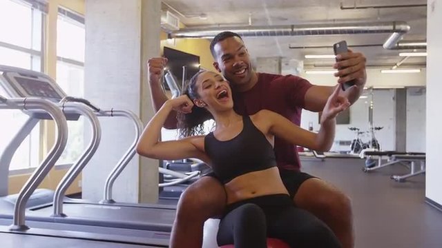 Cute Black and Hispanic couple smiling and taking goofy selfies together in gym after workout