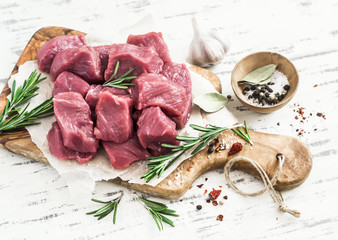 Fresh raw chopped beef, spices and herbs on an olive board on a light wooden background