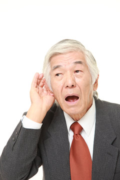 senior Japanese businessman with hand behind ear listening closely