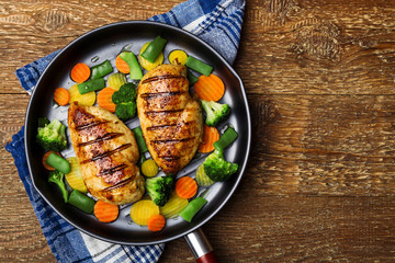 Grilled chicken breast with vegetables in a pan.