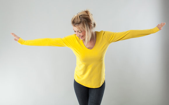 success concept - successful 20s blond woman with yellow shirt smiling with arms opened for theatre gesture or wellbeing,studio shot