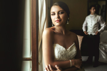 Gorgeous exotic french bride in white dress posing near window w