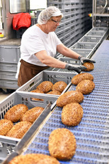 Frau arbeitet am Fliessband einer Großbäckerei - Auswahl und Versand von Broten // Woman working...