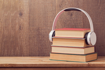 Audio books concept with stack of old book and headphones on wooden table