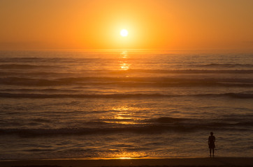 Sunset over the ocean with alone figure on the beach