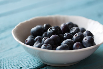 Closeup of fresh ripe blueberries in a bowl on a blue wooden background. Selective focus..