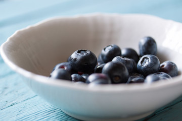 Closeup of fresh ripe blueberries in a bowl on a blue wooden background. Selective focus..