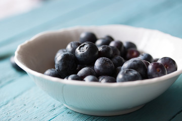 Closeup of fresh ripe blueberries in a bowl on a blue wooden background. Selective focus..