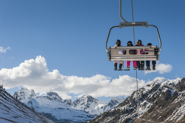 Chairlift full of skiers at a ski resort, with snowy mountains on background