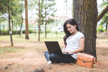 Young asian woman using a laptop while sitting outdoor in a park