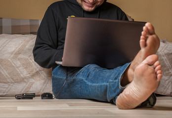 A happy barefoot man is  working on his laptop at home 
