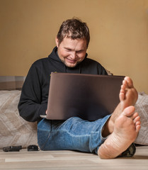 A happy barefoot man is  working on his laptop at home 