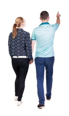 Back view of walking young couple (man and woman) pointing.