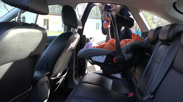 blond mother woman put baby safety chair with infant child on back car seat and fasten with safety belt. Safe baby transportation inside automobile. 4K UHD video clip.
