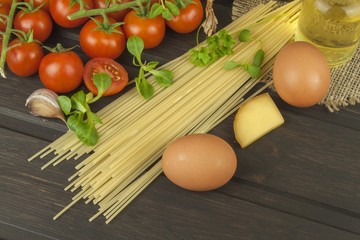 Preparing homemade pasta. Pasta and vegetables on a wooden table. Dietary food. Pasta, tomatoes, onion, olive oil and basil on wooden background. 
