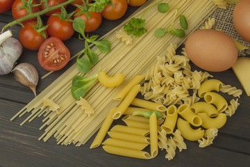 Preparing homemade pasta. Pasta and vegetables on a wooden table. Dietary food. Pasta, tomatoes, onion, olive oil and basil on wooden background. 
