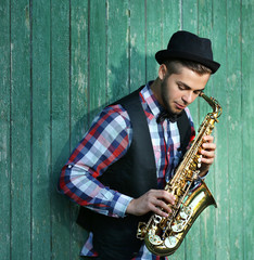 Fototapeta premium Young man playing on saxophone outside near the old wall
