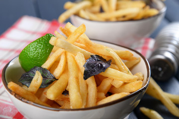 French fried potatoes in bowl with basil and sauce on old wooden background