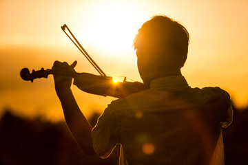 Young man or boy playing the violin at sunset - obrazy, fototapety, plakaty