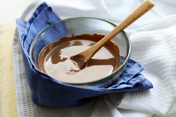 Melted chocolate in glass bowl, on wooden background