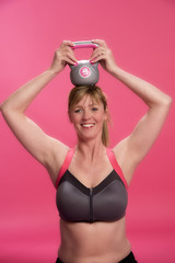 Woman wearing sports bra exercising with a kettle bell on her head