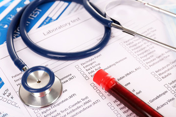 Blood in test tubes, stethoscope and investigation form on the table, close-up