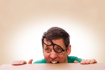 Mann mit Nerd Brille beißt in Tischkante