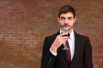 Man sniffing red wine in glass on brick wall background