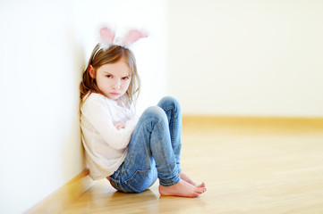 Very angry little girl wearing bunny ears sitting on a floor