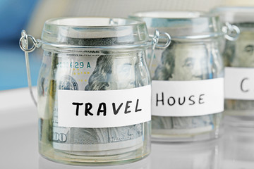 Glass jars with dollar banknotes for house and travel on a table