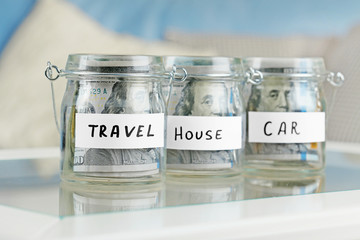 Glass jars with dollar banknotes for car, house and travel on a table