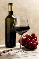 red wine glass with corkscrew, bottle and red grapes bunch