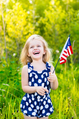 Laughing blond little girl with long curly hair holding american flag, outdoor portrait on sunny day in summer park. Independence Day, Flag Day concept