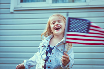 Cute little girl with long curly blond hair laughing and waving american flag. Independence Day,...