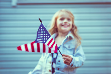 Flying american flag in little girl's hand. Selective focus, blurred background. Independence Day, Flag Day concept. Vintage and retro toning
