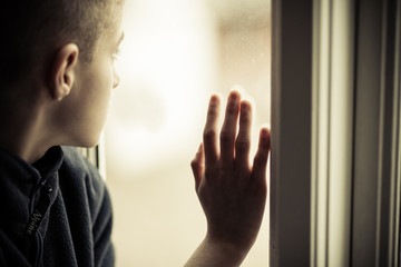 Sad Boy Looking Outside While Holding Glass Window
