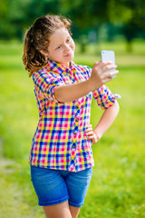 Lovely smiling girl posing and taking selfie with smartphone on sunny day in summer park. Teenage girl taking picture with smartphone